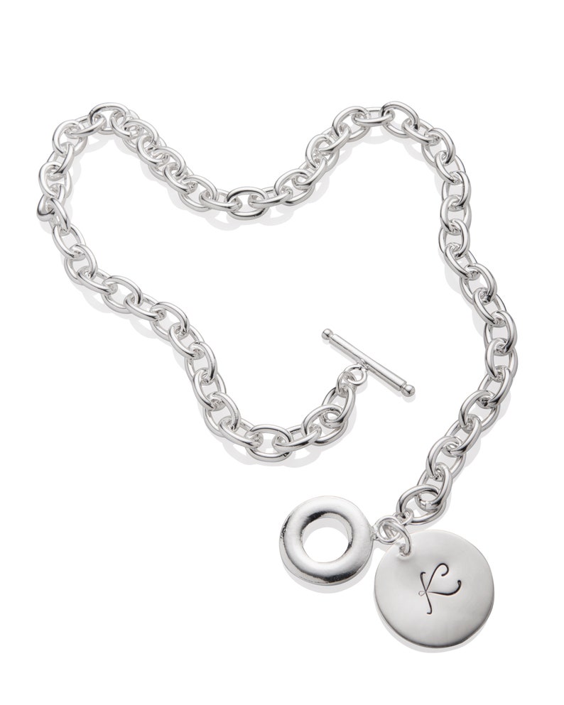 Puede incluir: Un collar de cadena de plata con un dije redondo grande y un dije redondo m&aacute;s peque&ntilde;o con la letra "K" grabada.