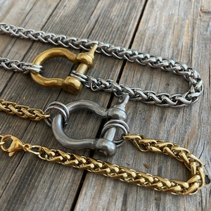 Pu&ograve; includere: Tre collane a catena diverse con finitura oro, argento e ottone. Ogni collana presenta una chiusura unica a forma di anello rotondo grande con un perno.