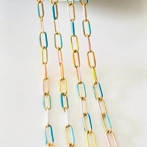 Op de afbeelding: Vijf strengen gouden ketting met kleurrijke emaille accenten. De kettingen zijn in tinten blauw, geel, roze en wit.