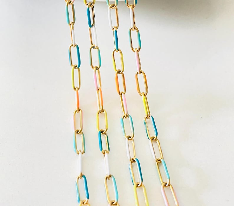 Op de afbeelding: Vijf strengen gouden ketting met kleurrijke emaille accenten. De kettingen zijn in tinten blauw, geel, roze en wit.