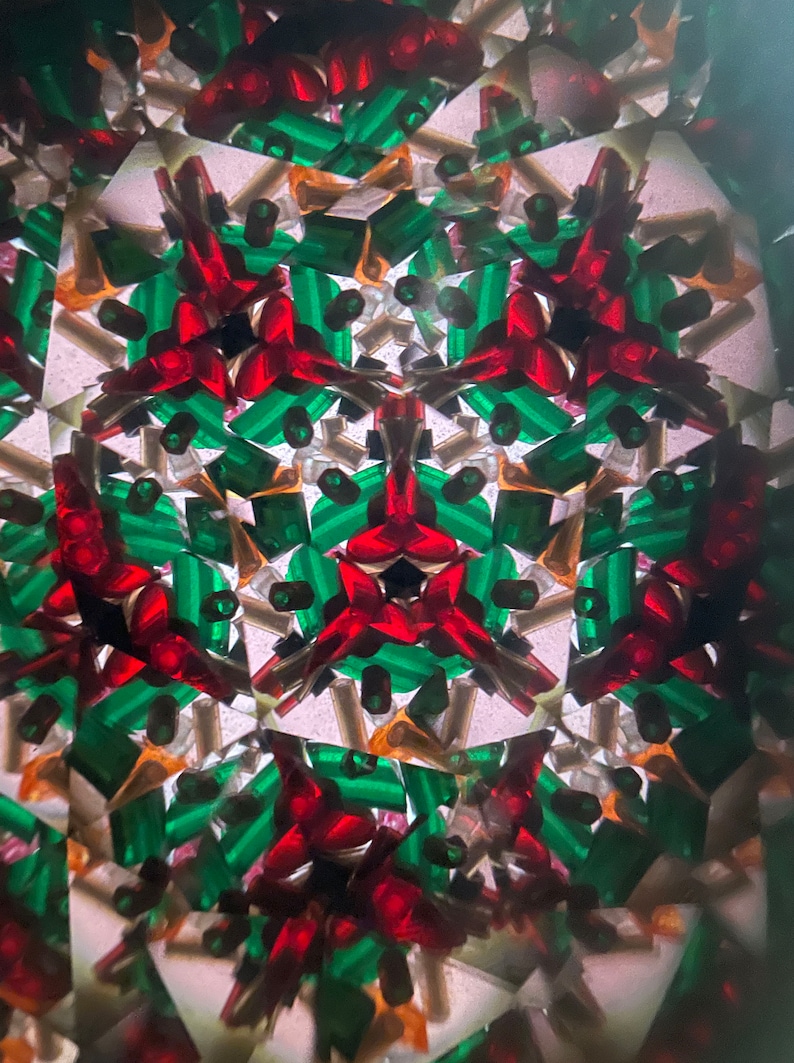K&ouml;nnte beinhalten: Ein Kaleidoskopbild mit einem symmetrischen Muster aus roten und gr&uuml;nen Formen. Der Hintergrund ist wei&szlig; mit einer subtilen Textur.