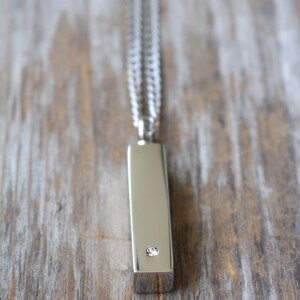 May include: A silver chain necklace with a silver bar pendant featuring a single clear diamond.