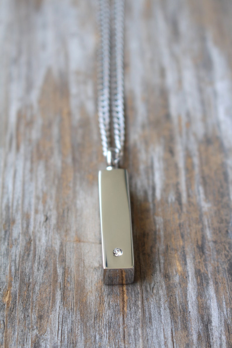 May include: A silver chain necklace with a silver bar pendant featuring a single clear diamond.
