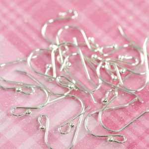 May include: A close-up of a pile of silver earring hooks on a pink and white checkered background.