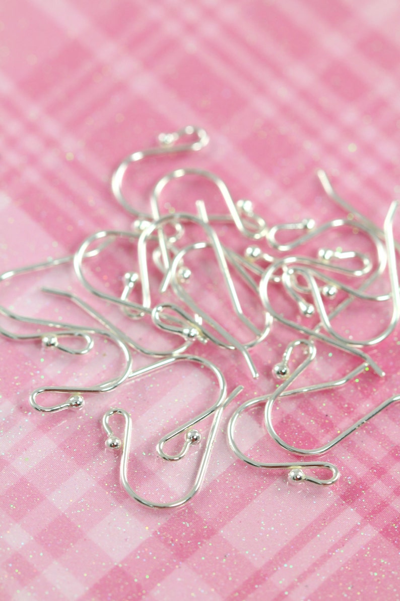 May include: A close-up of a pile of silver earring hooks on a pink and white checkered background.