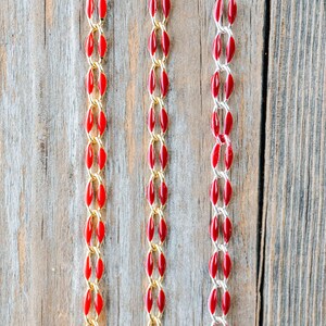 May include: Three strands of red and gold chain on a wooden background. The chains are made of small, oval-shaped beads.