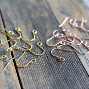 May include: Two sets of earring hooks, one set in gold and one set in rose gold. The hooks are made of metal and have a small ball at the end.