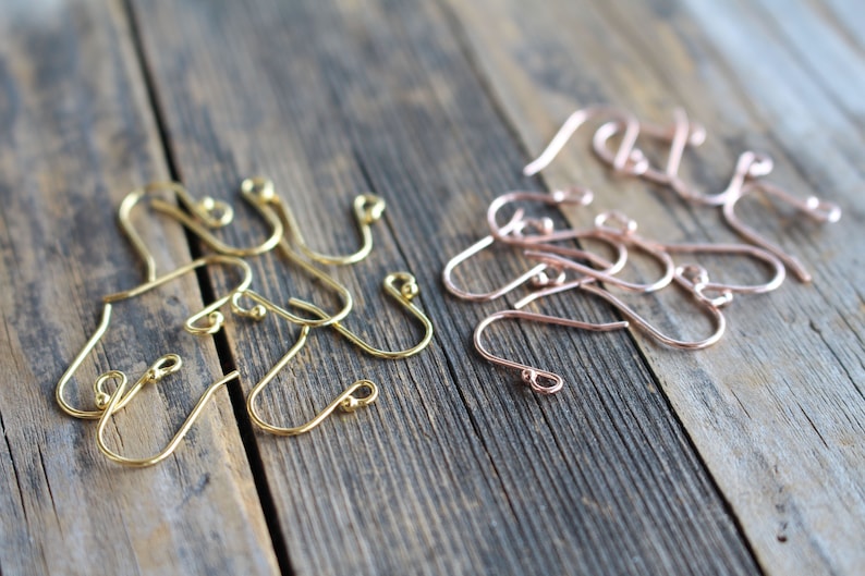May include: Two sets of earring hooks, one set in gold and one set in rose gold. The hooks are made of metal and have a small ball at the end.