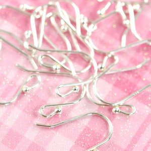 May include: A close-up of a pile of silver earring hooks on a pink sparkly background.