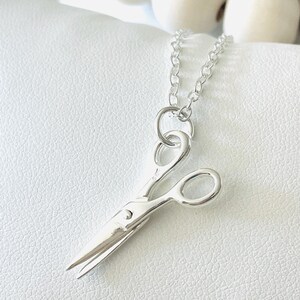 May include: A silver necklace with a small, detailed pair of scissors pendant.