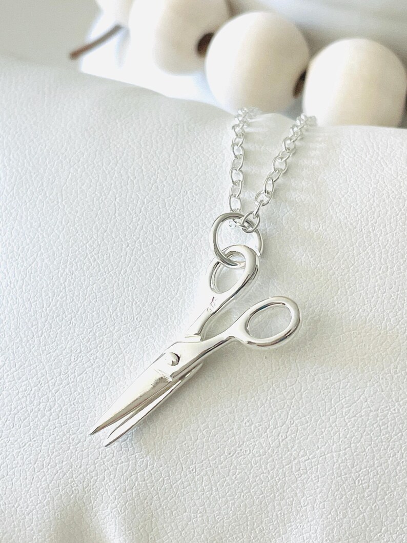May include: A silver necklace with a small, detailed pair of scissors pendant.