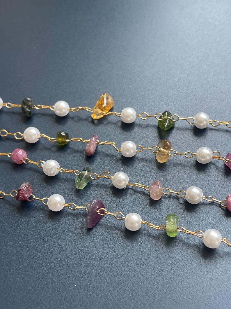 Puede incluir: Primer plano de varias hebras de joyer&iacute;a delicada. Cada hebra presenta peque&ntilde;as perlas blancas y brillantes intercaladas con piedras preciosas de colores de forma irregular en tonos verdes, amarillos, rosas y morados. Las cuentas est&aacute;n ensartadas en finas cadenas de oro.