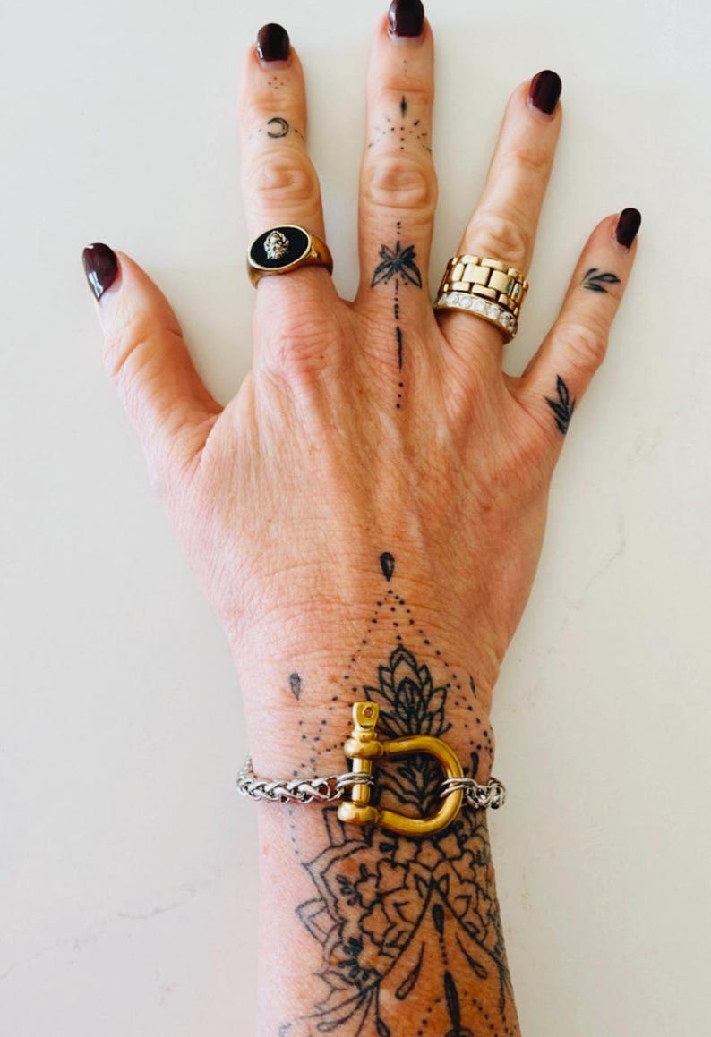 Pu&ograve; includere: Un braccialetto d'oro con una grande chiusura a forma di U in oro. Il braccialetto &egrave; fatto di una catena d'argento. Il braccialetto &egrave; al polso di una persona, che ha diversi piccoli tatuaggi neri.