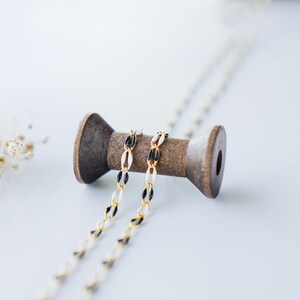 May include: A gold and black chain necklace wrapped around a wooden spool. The spool is on a white surface.