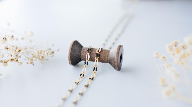 May include: A gold and black chain necklace wrapped around a wooden spool. The spool is on a white surface.