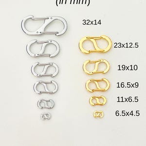 May include: A set of 10 silver and gold lobster clasps in various sizes, ranging from 6.5 x 4.5 mm to 32 x 14 mm. The clasps are arranged in two rows, with the silver clasps on the left and the gold clasps on the right. The text "(in mm)" is printed above the clasps, and the dimensions of each clasp are printed next to it.
