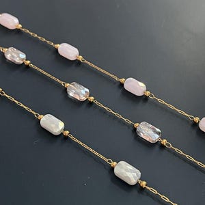 May include: Close-up of several delicate necklaces. Each necklace features a gold chain with alternating faceted, rectangular beads in shades of pink, clear, and white. Small gold beads accent the design, creating a refined and elegant look.