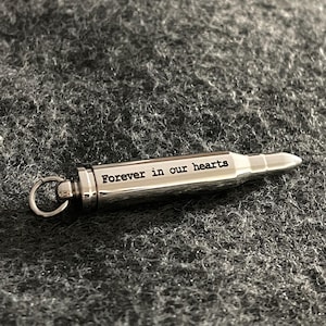 Puede incluir: Un llavero de plata con forma de bala con la inscripci&oacute;n "Forever in our hearts".