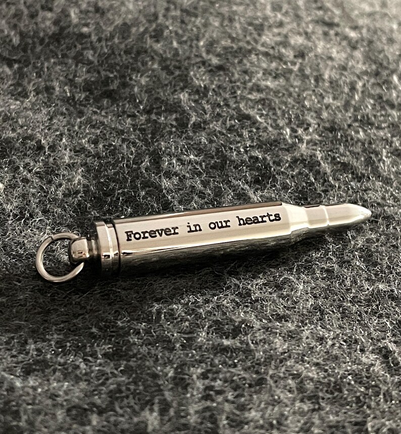 Puede incluir: Un llavero de plata con forma de bala con la inscripci&oacute;n "Forever in our hearts".