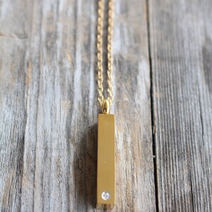 May include: A gold chain necklace with a gold bar pendant featuring a single clear rhinestone.