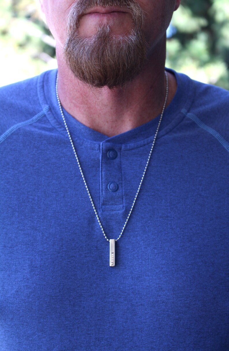 May include: A silver chain necklace with a silver bar pendant engraved with the word "Kiley".