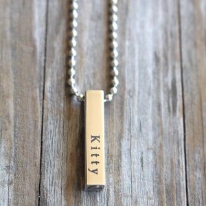 May include: A silver chain necklace with a silver bar pendant engraved with the word "Kitty".