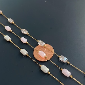 May include: Close-up of three delicate gold necklaces. Each necklace features a chain with alternating clear, pink, and white iridescent rectangular beads. A penny is included for scale, showing the necklaces' fine detail.