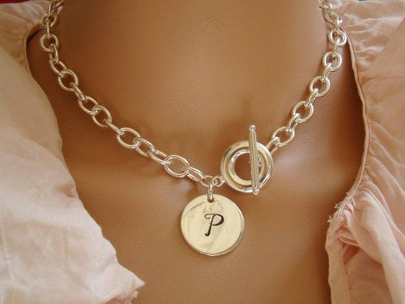 Puede incluir: Un collar de cadena de plata con cierre de palanca y un colgante redondo con la letra "P" grabada.