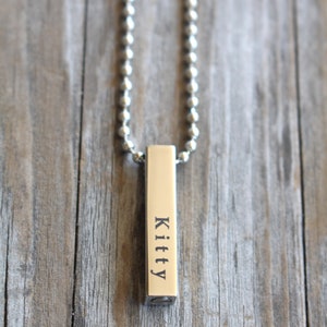 May include: A silver chain necklace with a silver bar pendant engraved with the name "Kitty".