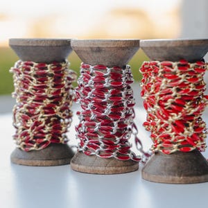 May include: Three spools of red and gold chain, each wound around a wooden spool.