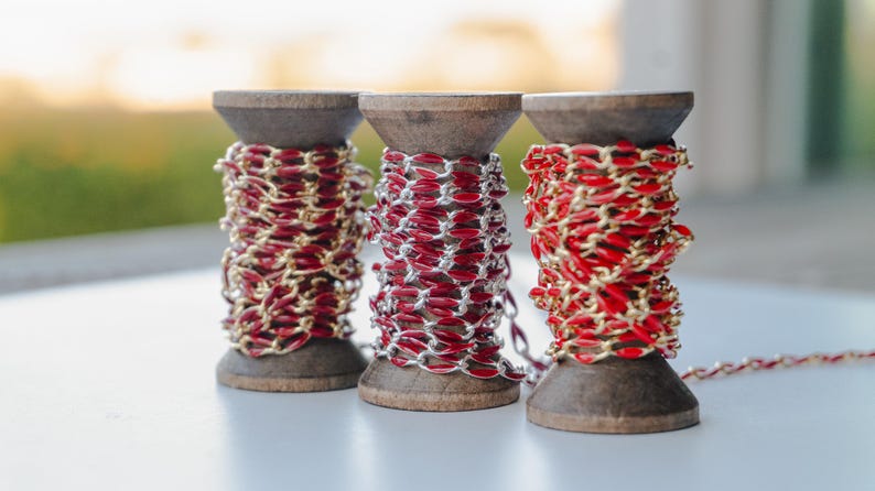 May include: Three spools of red and gold chain, each wound around a wooden spool.
