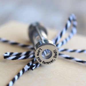 May include: A silver metal keepsake container with a clear glass vial inside. The container has an inscription that reads "Love you forever, Dad".