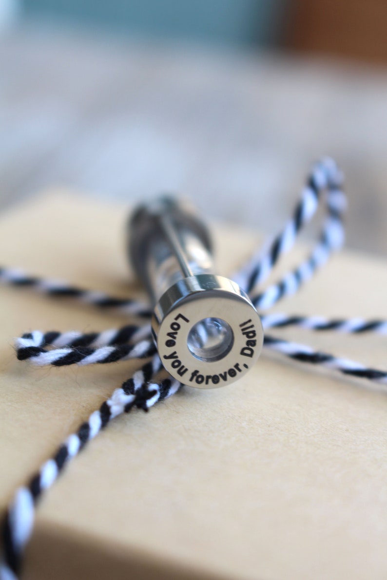 May include: A silver metal keepsake container with a clear glass vial inside. The container has an inscription that reads "Love you forever, Dad".