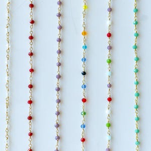 May include: A variety of gold chains with different colored beads. The chains are all the same length and are hanging from a white background.