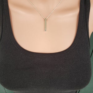May include: A silver chain necklace with a long, thin, silver bar pendant.