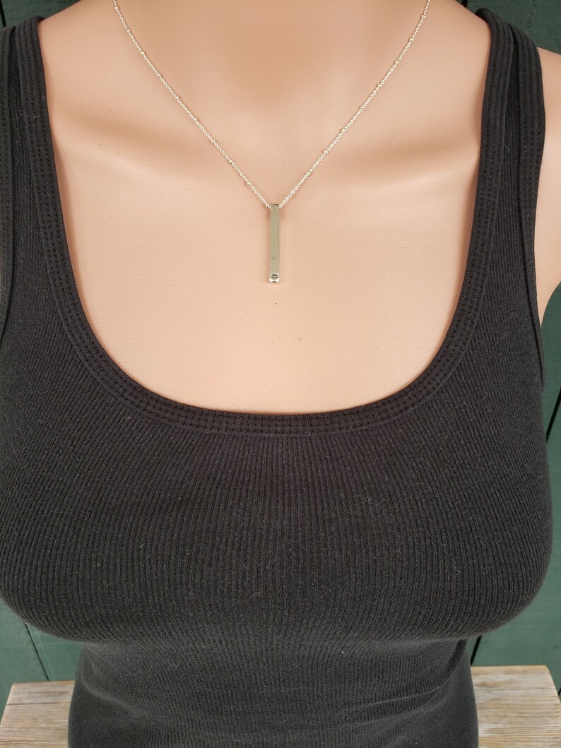 May include: A silver chain necklace with a long, thin, silver bar pendant.