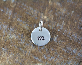 May include: A silver charm with the letter "m" engraved on it.