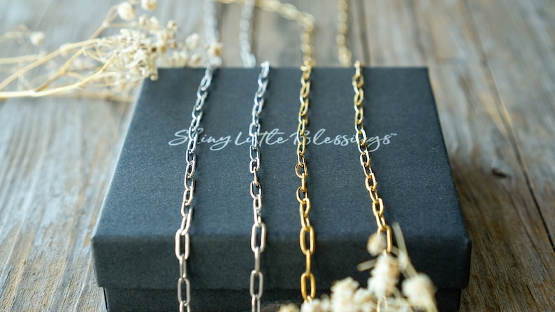 May include: Three silver, gold, and black chains on a black box with the text "Shiny Little Blessings" printed on the box.