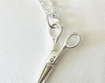 Op de afbeelding: Een zilveren ketting met een kleine, gedetailleerde hanger in de vorm van een schaar.