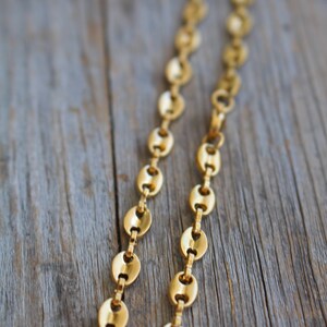 May include: A gold chain necklace with oval-shaped links. The chain is lying on a wooden surface.