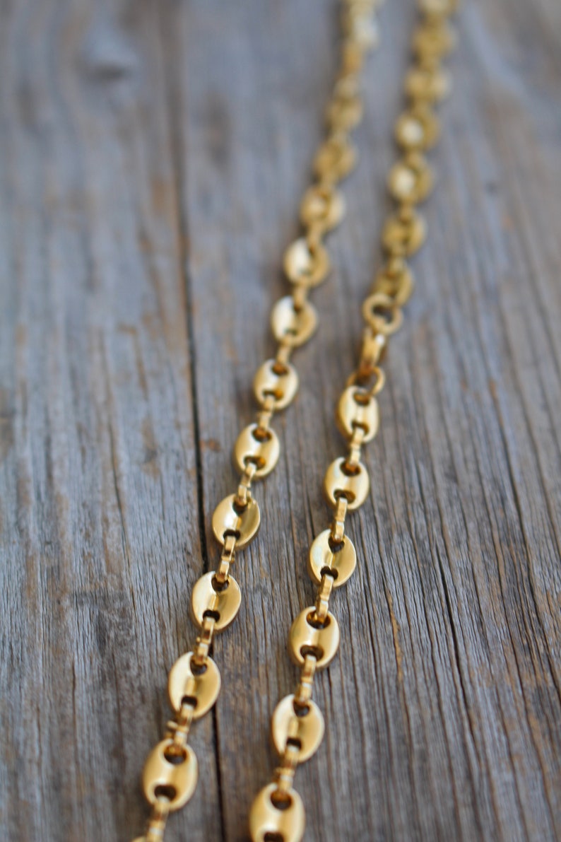 May include: A gold chain necklace with oval-shaped links. The chain is lying on a wooden surface.