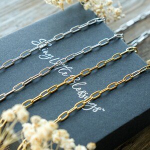 May include: Three silver, gold, and silver chains on a black box with the text "Simply Little Blessings" printed on the box.