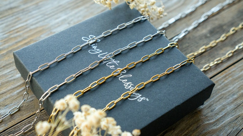 May include: Three silver, gold, and silver chains on a black box with the text "Simply Little Blessings" printed on the box.