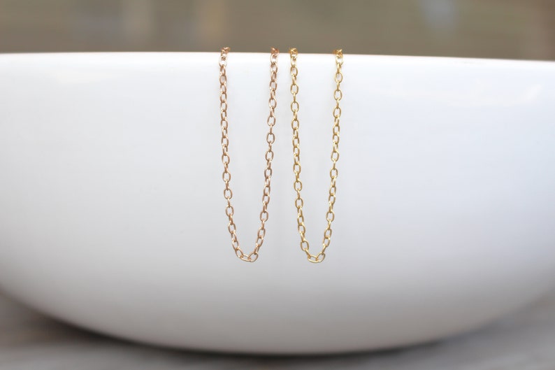 May include: Two gold chains, one slightly thicker than the other, are hanging from the edge of a white bowl.