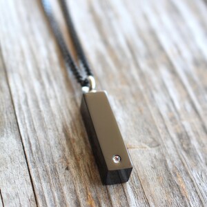 May include: A black necklace with a black rectangular pendant featuring a small clear rhinestone.