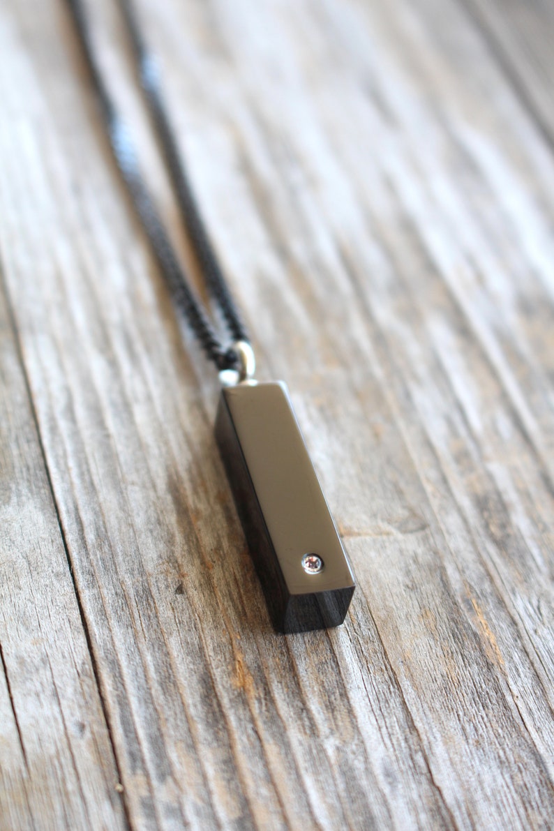 May include: A black necklace with a black rectangular pendant featuring a small clear rhinestone.