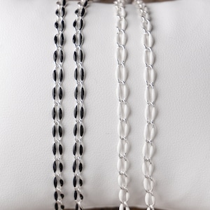 Könnte beinhalten: Zwei silberne Ketten mit ovalen Gliedern, eine mit schwarzer Emaille und eine mit weißer Emaille.