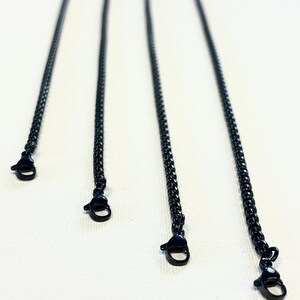 May include: Four black chain necklaces with lobster claw clasps are displayed against a white backdrop. The chains are evenly spaced and angled, creating a sense of depth. These chains are likely for jewellery making or as necklace components.