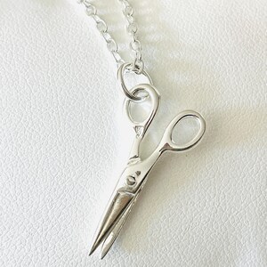 May include: A silver necklace with a small, detailed charm of a pair of scissors.