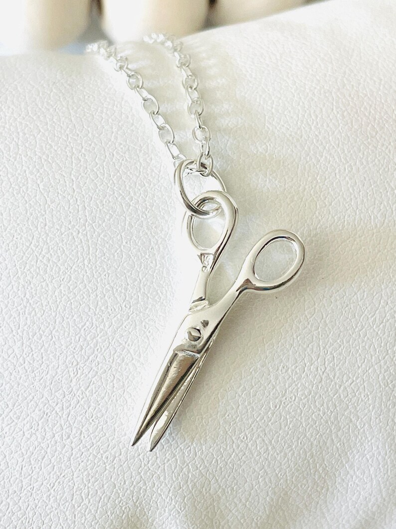May include: A silver necklace with a small, detailed charm of a pair of scissors.
